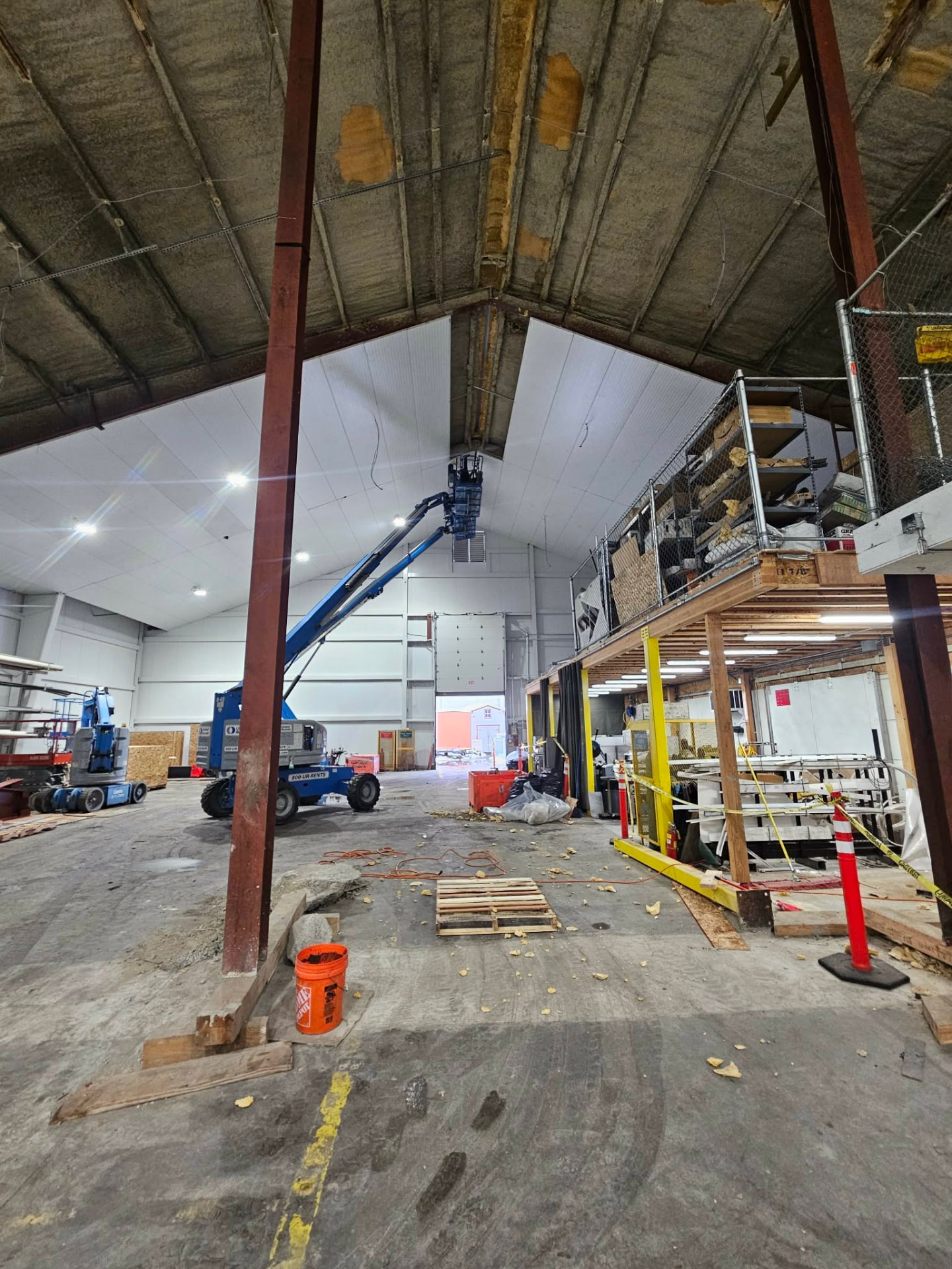 White commercial ceiling liner panels being installed with a boom lift beneath exposed roof insulation